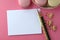 Top view of blank note card, laptop, cell phone and French macarons on pink background. Feminine workspace desktop with copy space