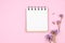 Top view of blank notebook with purple flower on pink background