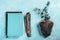 Top view of blue and brown notebooks, and fineliner markers on piece of wood and green eucalyptus plants on turquoise