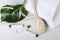 Top view of bottles of moisturizer cream, cosmetic products, white towels, body brush and green leaf on the white marble surface