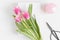 Top view of bouquet of pink tulips, book and  workspace accessories on a white table
