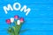 top view of bouquet of pink and white tulips and word mom on blue table, mothers day concept