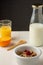 Top view of bowl with cereals, bottle of milk, half orange, glass with juice and spoon on white wooden table, black background,