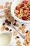 Top view of bowl with cereals, red berries, spoon and jug with milk, on white marble table