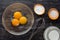 Top view of bowl with three yolks, starch, sugar and milk and whisk as ingredients to make custard cream on the black background