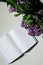 Top view of bright branch of lilac with open diary on white table on grey curtains background