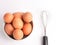 Top view a bunch of chicken eggs in a bowl with egg beater isolated on white background.