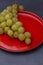 Top view of bunch of green grapes on red plate and dark background, in vertical, with selective focus, in Madrid, Spain