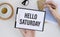 Top view of a business card with text Hello Saturday, pen, cup coffee on a colored background.