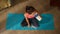 Top view capturing a young woman sitting on a mat in a lotus pose, drinking a protein shake from a bottle. Home, room