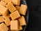 Top view of caramel vanilla fudge candies on a black textured ceramic plate over dark wood table. Fresh tasty chewy bonbons made