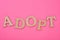 Top view of cardboard word adopt on bright pink background.