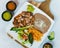 Top view of carnitas plate on a wooden board with refried beans, rice, salsa, and lime