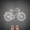 Top view of casual man\'s shoes and a sketched model of a bicycle on asphalt. A concept of environmental friendly way of travelling