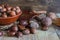 Top view of chestnuts with leaves and ceramic bowl with hazelnuts in the background, on weathered wooden background