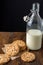 Top view of chocolate chip cookies on brown paper and dark wooden table with bottle of milk, black background