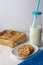 Top view of chocolate chip cookies on white plate with blue knit blanket, bottle of milk with straw and metal box with cookies, on