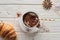 Top view of Christmas cacao in mug with decoration near croissant on white wooden table.
