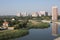 Top view of the city. Blue river with green banks and a reflection of a tall building in it.