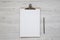 Top view, clipboard with blank sheet of paper and pencil over white wooden background. Flat lay, overhead