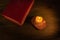 Top view of a closed bible illuminated with a lit candle on a wooden background