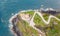 Top view of the coastline with the red topped lighthouse and the winding road to it, surrounded by the ocean