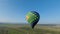 Top view of colorful balloon in sky. Shot. Multi-colored balloon is flying over green fields. Hot air balloon flight at