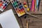 Top view of colorful paint palettes, paintbrushes, color pencils and blank sketch pad on wooden surface.