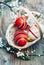 Top view of colorful painted easter eggs in basket and cherry blossom branch decor on vintage wooden table. Traditional seasonal