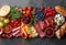 Top view continental breakfast - colorful variety of fruits, berries, cheeses, cold cuts and bread on a dark background