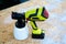 Top view cordless paint sprayer gun with full container of white paint on oriented strand board OSB board wood panel