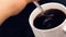 Top of view of cup of black coffee with adult hand that use a spoon inside, on black wood table