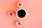 Top view of a cup of black coffee and around are three donuts with pink icing on a pink background. Place for text. Pause for