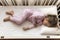 top view Cute little 3-4 years preschool baby girl kid sleeping sweetly in white crib during lunch rest time in pink