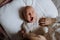 Top view of cute little baby yawning in bed, big sister holding newborn hand. Sisterly love, joy for new family member.