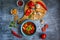 Top view of a cutting board with chopped pepper, garlic, a blue plate with appetizing soup, tomatoes and a bowl of crackers on a