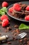 Top view of dark plate with pieces of brownie with raspberries, mint leaves and fork, with selective focus, on dark table
