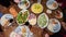 Top view of a dining table with various delicious dishes. The hands of unrecognizable people pour food into their plates