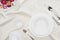 Top view of dishware with glasses, coffee cup and bouquet on white tablecloth