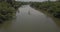 Top view drone getting close to little white boat cruising along big beautiful calm jungle river with green palm trees.