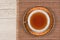 Top view of an east style painted cup with tea on a saucer located on a bamboo mat on a wooden background