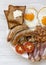 Top view English breakfast with fried eggs, bacon, sausages, beans and toasts. White wooden background. Copy space and text area