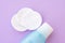 Top view of facial toner and round cotton pads on purple background with copy space. Blue liquid tonic or make up remover for face