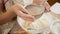 Top view of female baker sifting flour with sieve in big glass bowl for making dough.