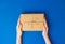 Top view of female hands holding present box package on Blue background. Zero waste shopping concept. Flat lay banner, top view,