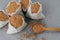 Top view of five small sacks filled with raw buckwheat, wooden spoon near with uncooked cereals, dark background. Healthy food