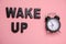 Top view flat lay wake up message and black clock on a pastel pink background