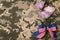 Top view of flowers and ribbon bow with American flag pattern on camouflage background. Armed Forces Day