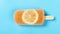 Top view fresh grapefruit flavor popsicle with slice of lemon melting timelapse on a blue background