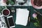 Top view of fresh rose placed next to blank paper on marble desk with green cloth with empty screen phone, cup with tea and watch